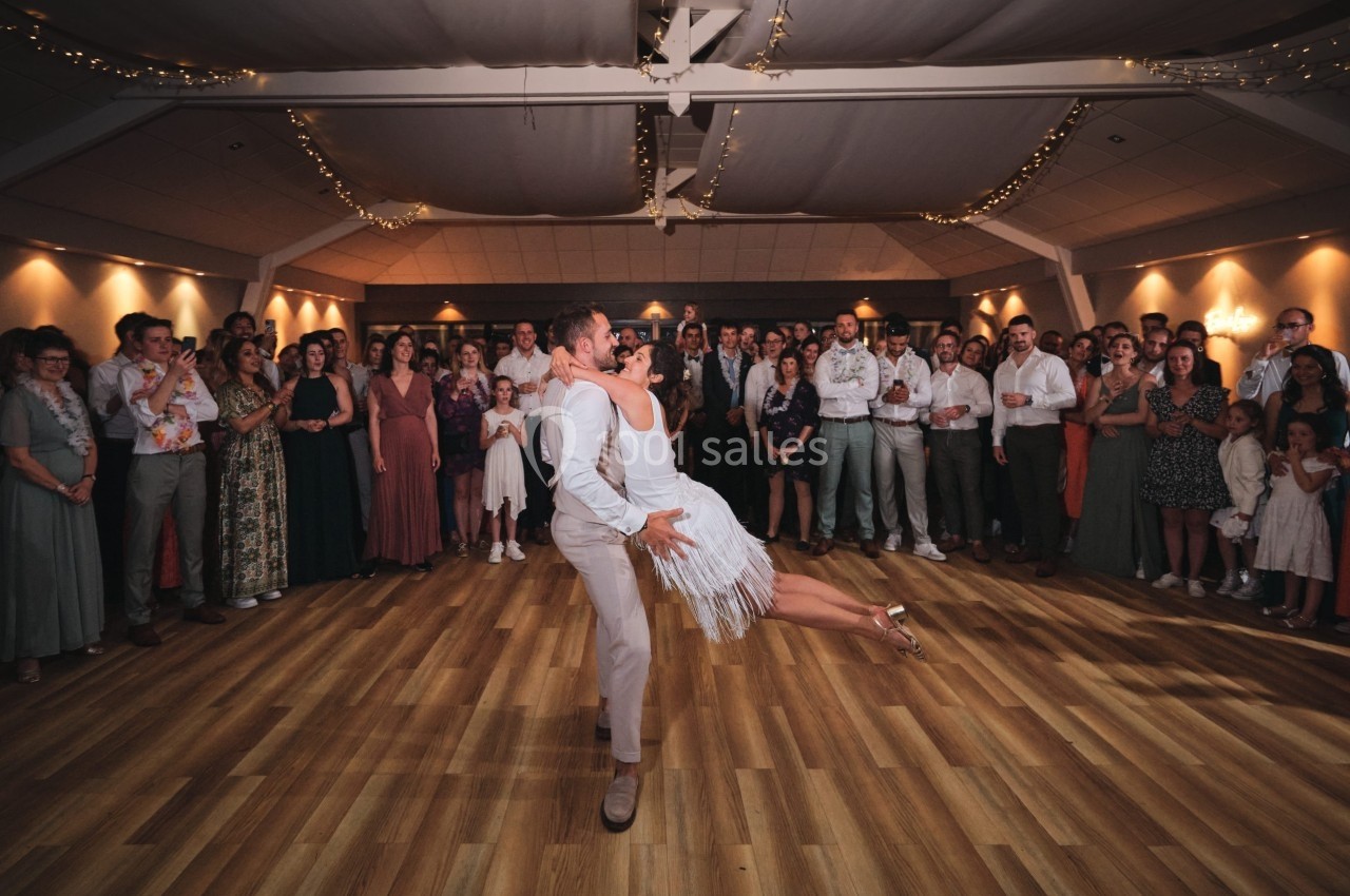 Un couple danse au centre d'une salle décorée, entouré d'invités qui les regardent avec attention.