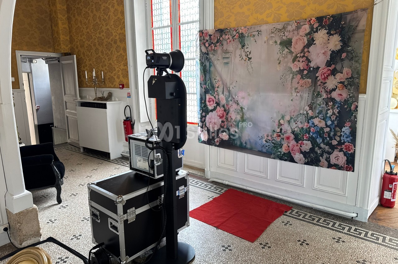 Appareil photo professionnel monté sur un trépied devant un fond floral dans une pièce au décor classique.