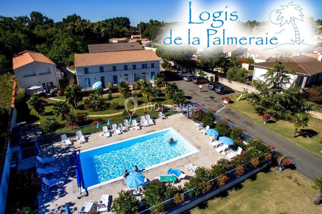 Vue aérienne d'une résidence avec piscine, transats, parasols, espaces verts et bâtiments environnants.