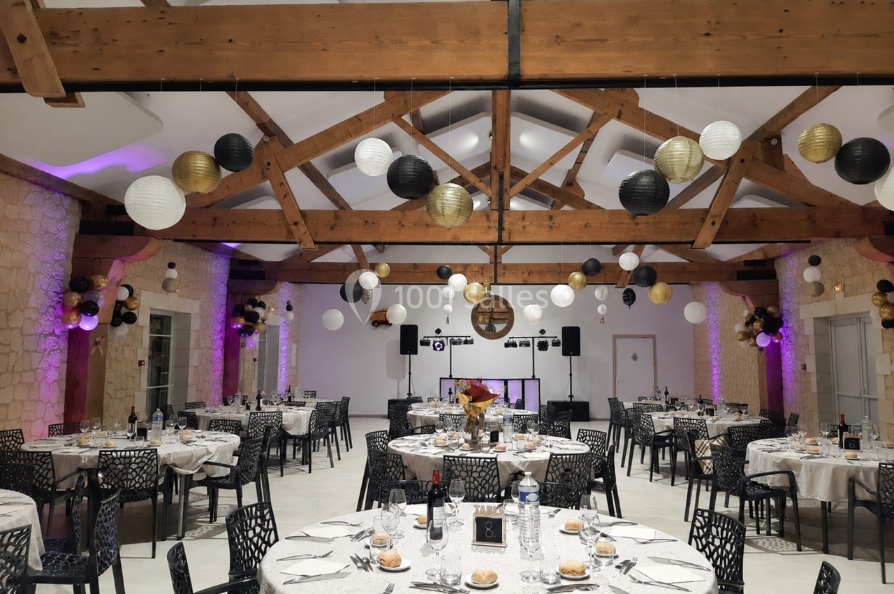Salle de réception décorée avec des lanternes suspendues, tables dressées et éclairage chaleureux.