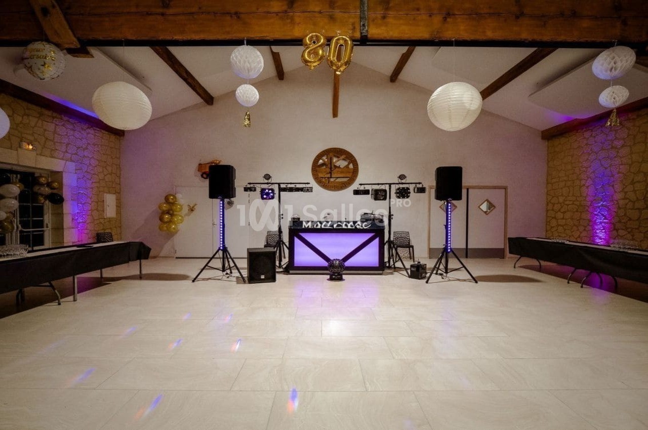 Salle de réception décorée avec des guirlandes lumineuses, des ballons dorés et une table de DJ au centre.