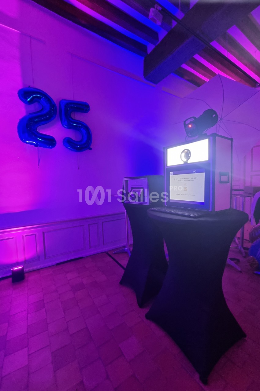Borne photo rétro-éclairée dans une salle décorée avec des ballons ’25’ et un éclairage violet.