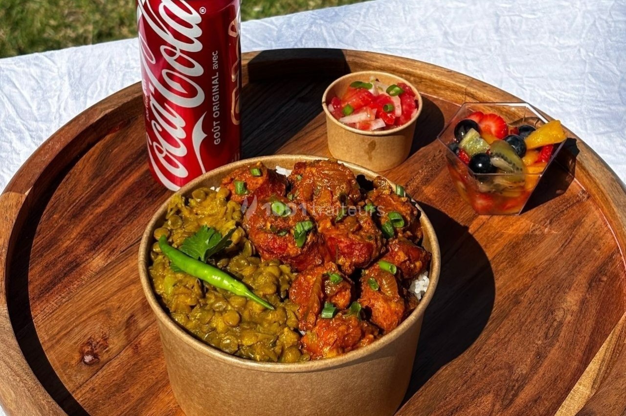 Repas servi sur un plateau rond avec un bol de curry, des lentilles, une salade de fruits, une salsa et une canette de soda.