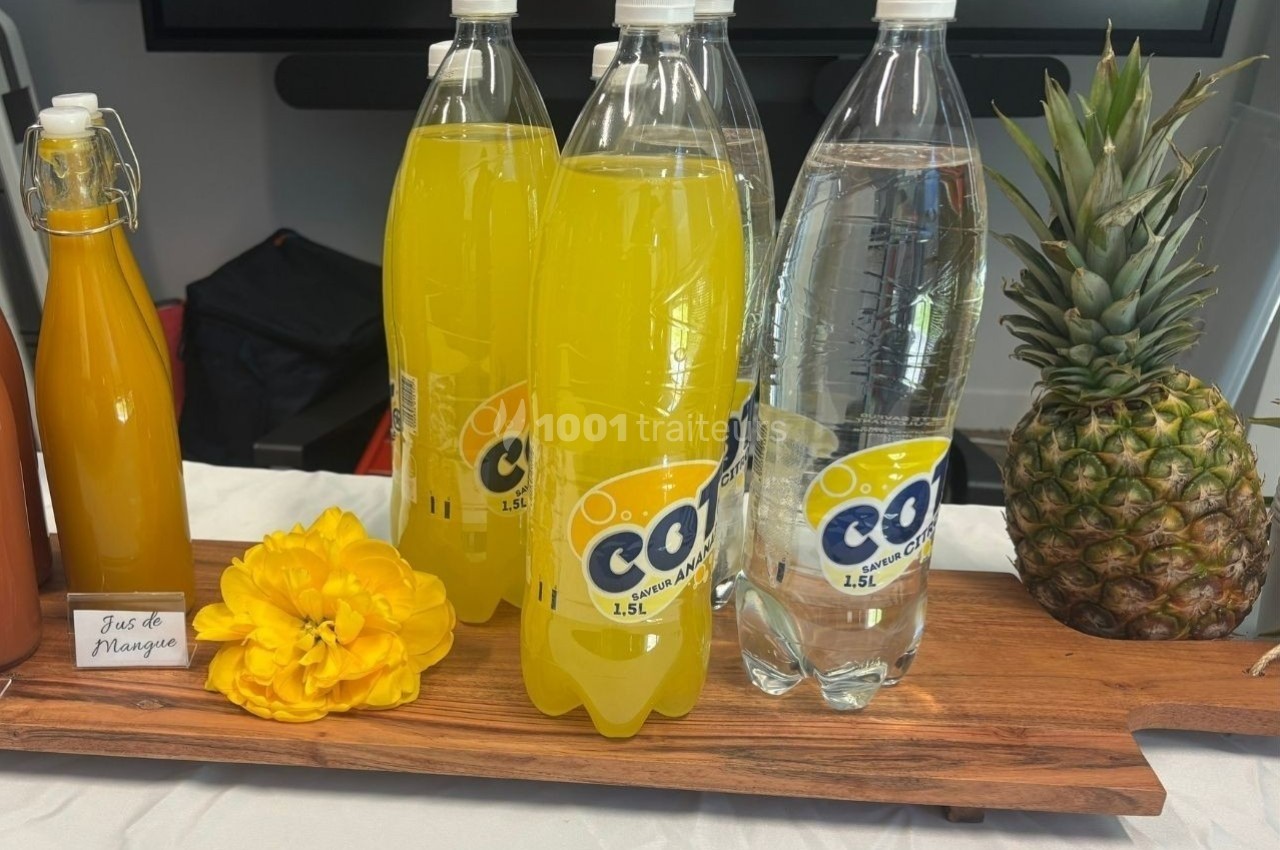 Bouteilles de soda et d'eau pétillante sur une planche en bois, avec un ananas et une fleur jaune en décoration.