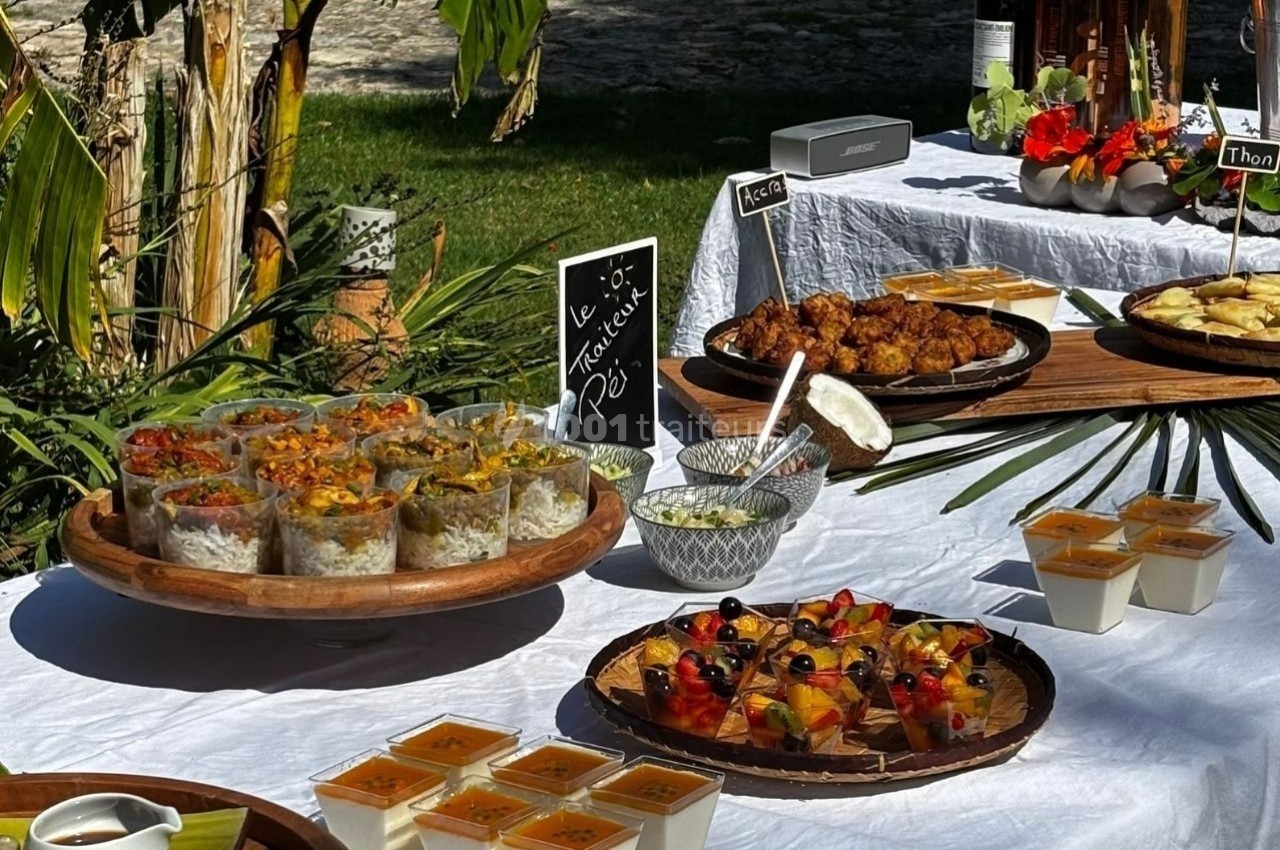 Buffet en extérieur avec verrines, desserts, fruits et plats variés disposés sur une nappe blanche.