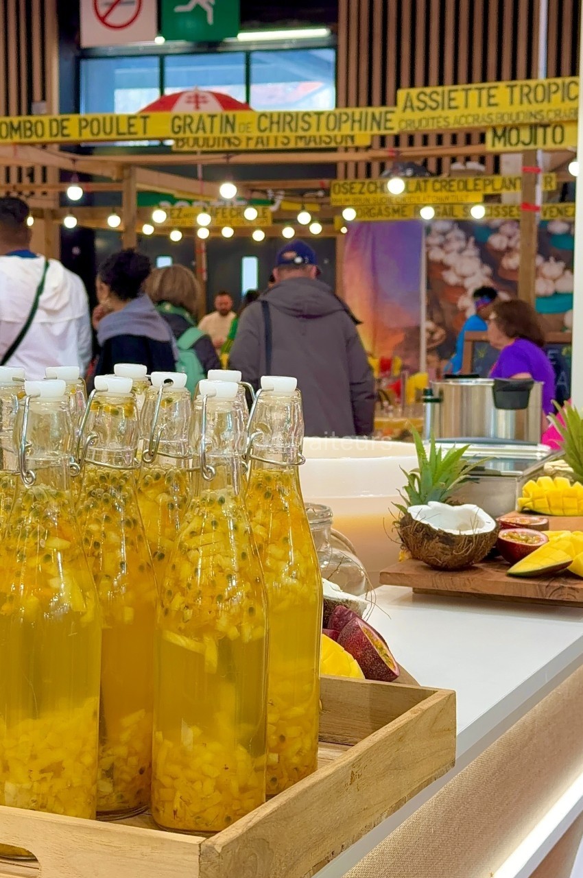 Bouteilles remplies de boisson jaune avec morceaux de fruits, posées sur un comptoir, foule en arrière-plan.