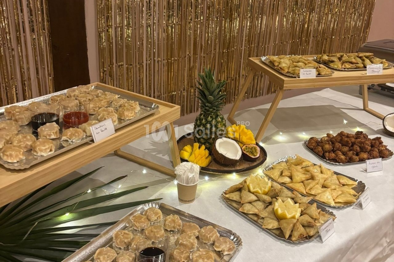 Buffet avec assortiment de samoussas, bouchées vapeur, fruits tropicaux et sauces, présenté sur des plateaux.