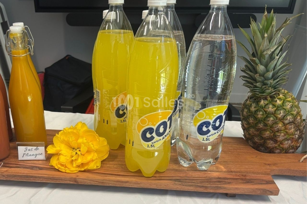 Bouteilles de soda jaune et d'eau pétillante sur une planche en bois, avec une fleur jaune et un ananas à côté.