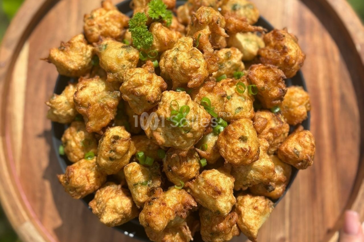 Assiette de beignets dorés garnis de ciboulette, présentée sur un plateau en bois.