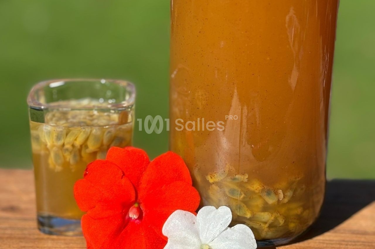 Boisson orange dans une carafe et un verre, avec des graines visibles, décorée de fleurs rouges et blanches sur une table en…