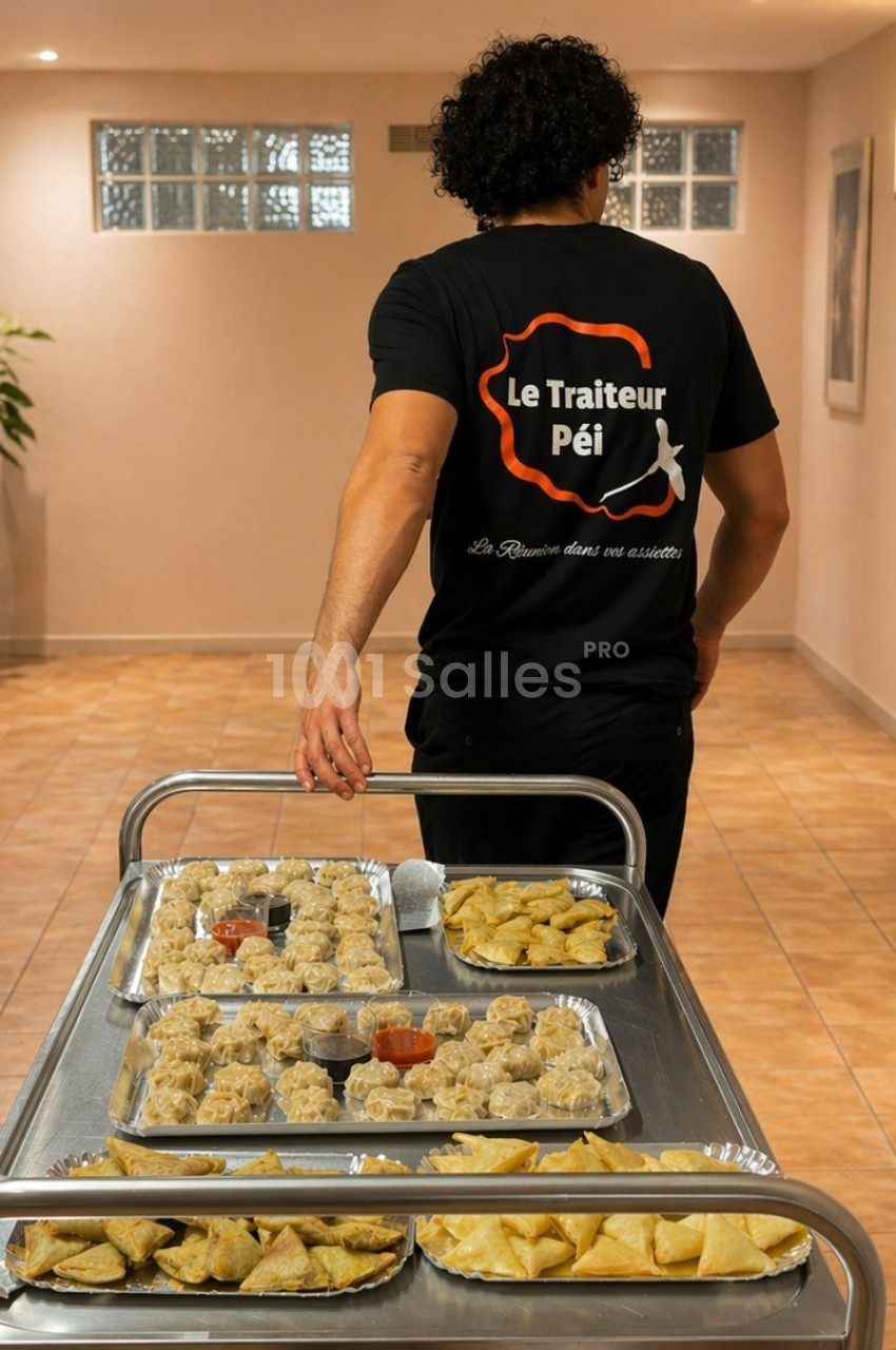Un traiteur transporte un chariot rempli de plateaux contenant des bouchées et amuse-bouches dans un couloir.