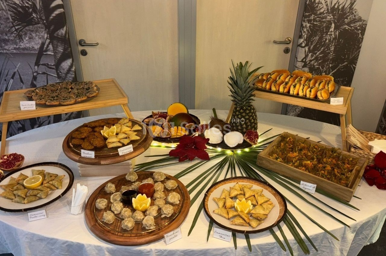 Table garnie de divers plats et desserts exotiques, présentés sur des plateaux en bois avec des décorations tropicales.
