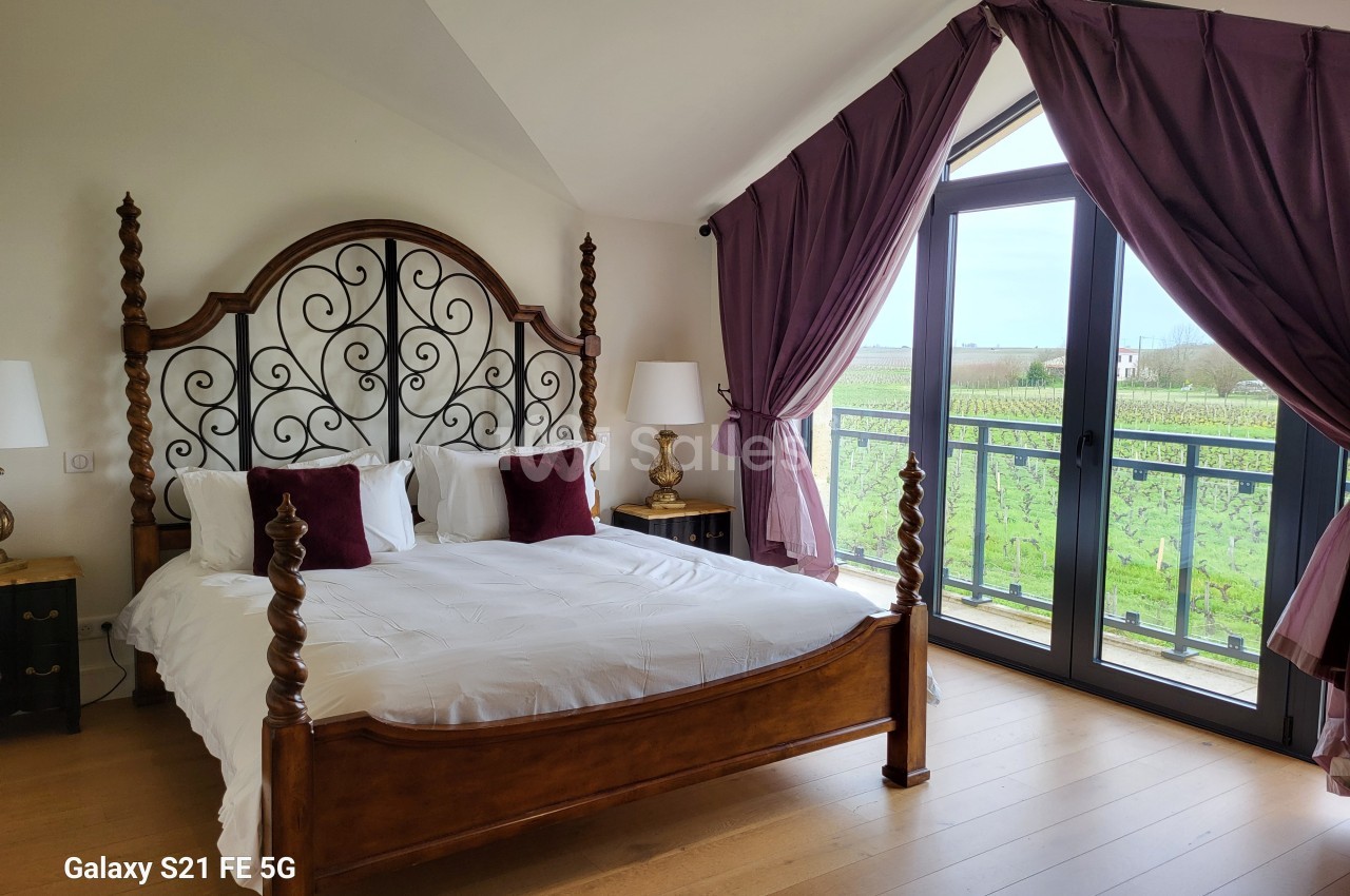 Chambre lumineuse avec lit double en bois sculpté, grandes fenêtres donnant sur un paysage de vignes.