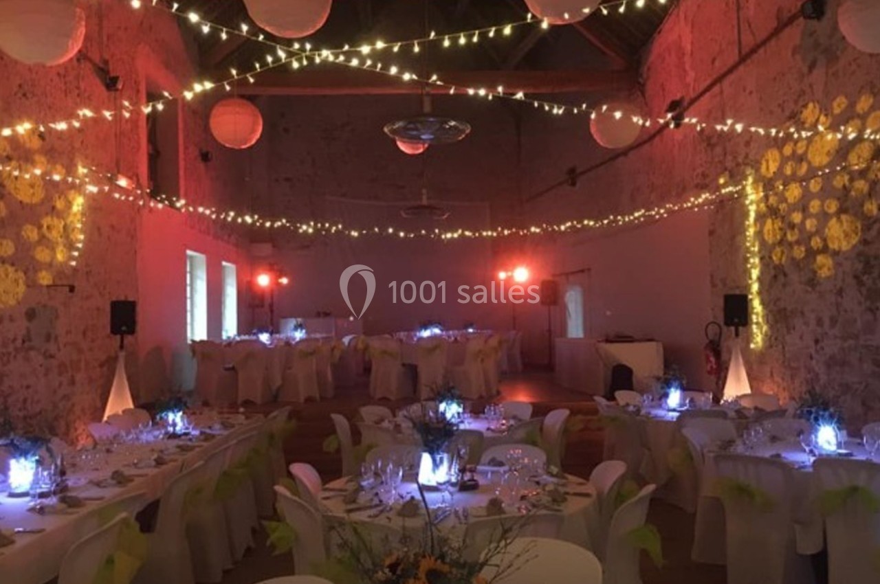 Salle de réception décorée avec des guirlandes lumineuses, des tables dressées et une ambiance tamisée.