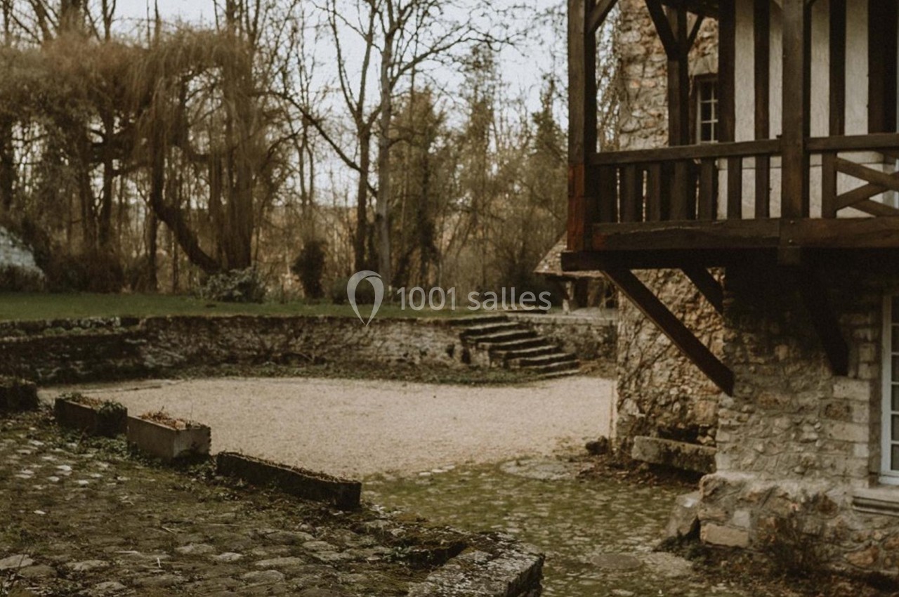 Cour extérieure pavée avec escaliers en pierre, entourée de végétation et d'une maison à colombages.