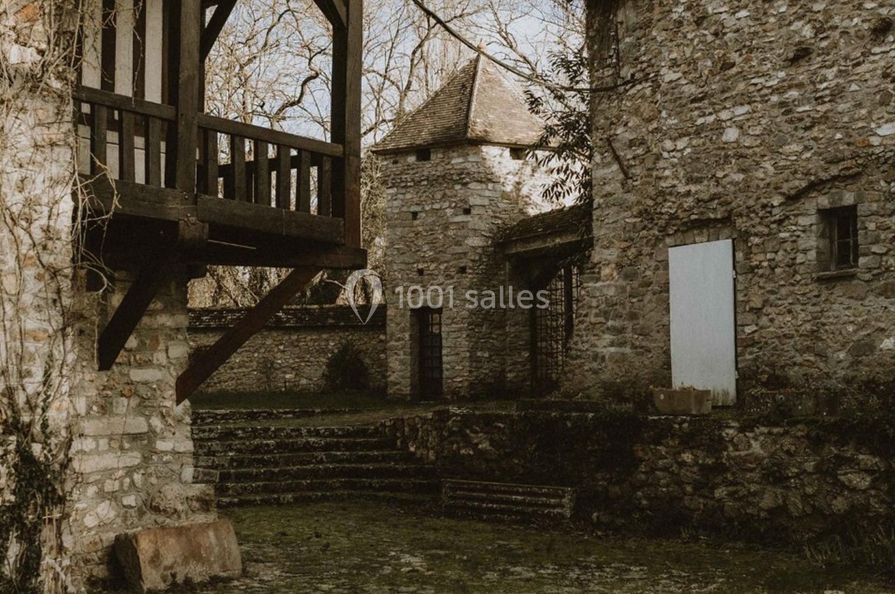 Cour intérieure d'un bâtiment en pierre avec escaliers, murs anciens et végétation discrète en arrière-plan.