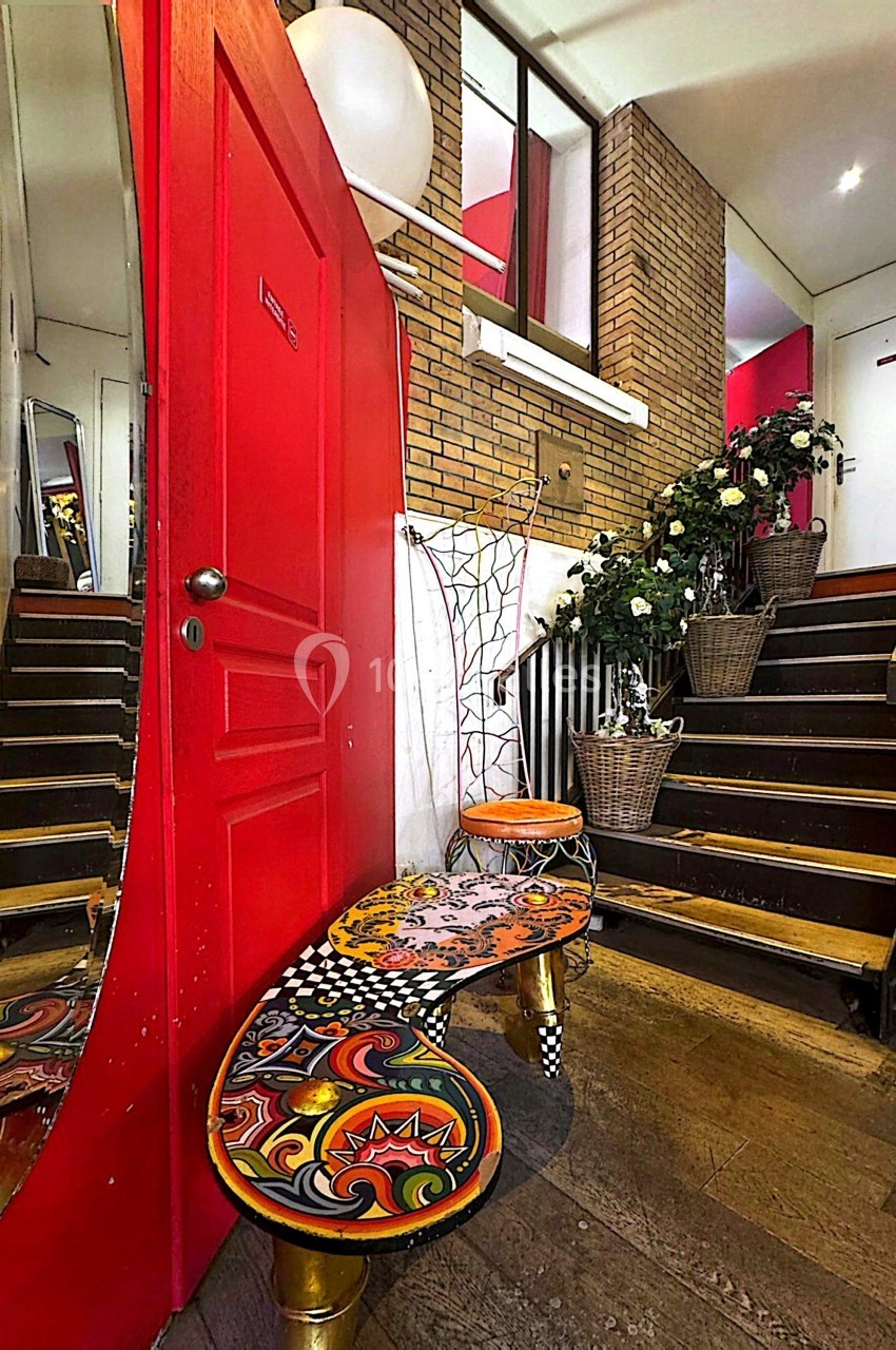 Escalier intérieur avec murs en briques, porte rouge, banc coloré et plantes en pots décorant l'espace.