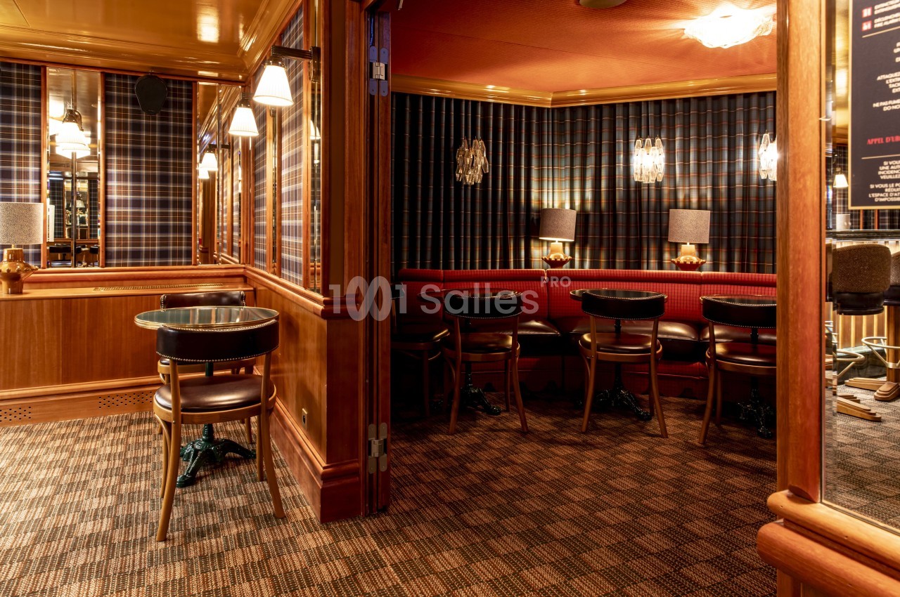Salle avec tables et chaises en bois, banquettes rouges, murs à motif écossais et éclairage tamisé.