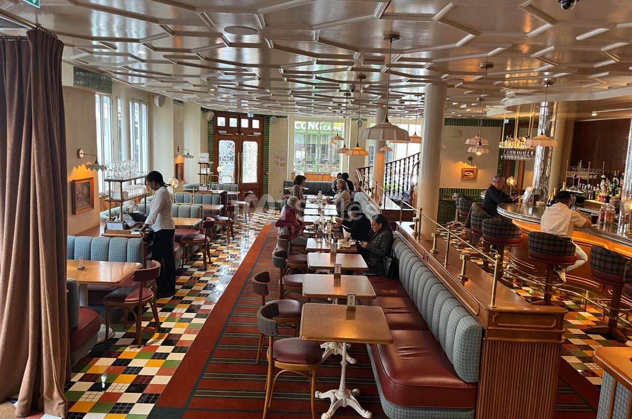 Salle de restaurant lumineuse avec des tables en bois, banquettes colorées et un sol à motifs géométriques.