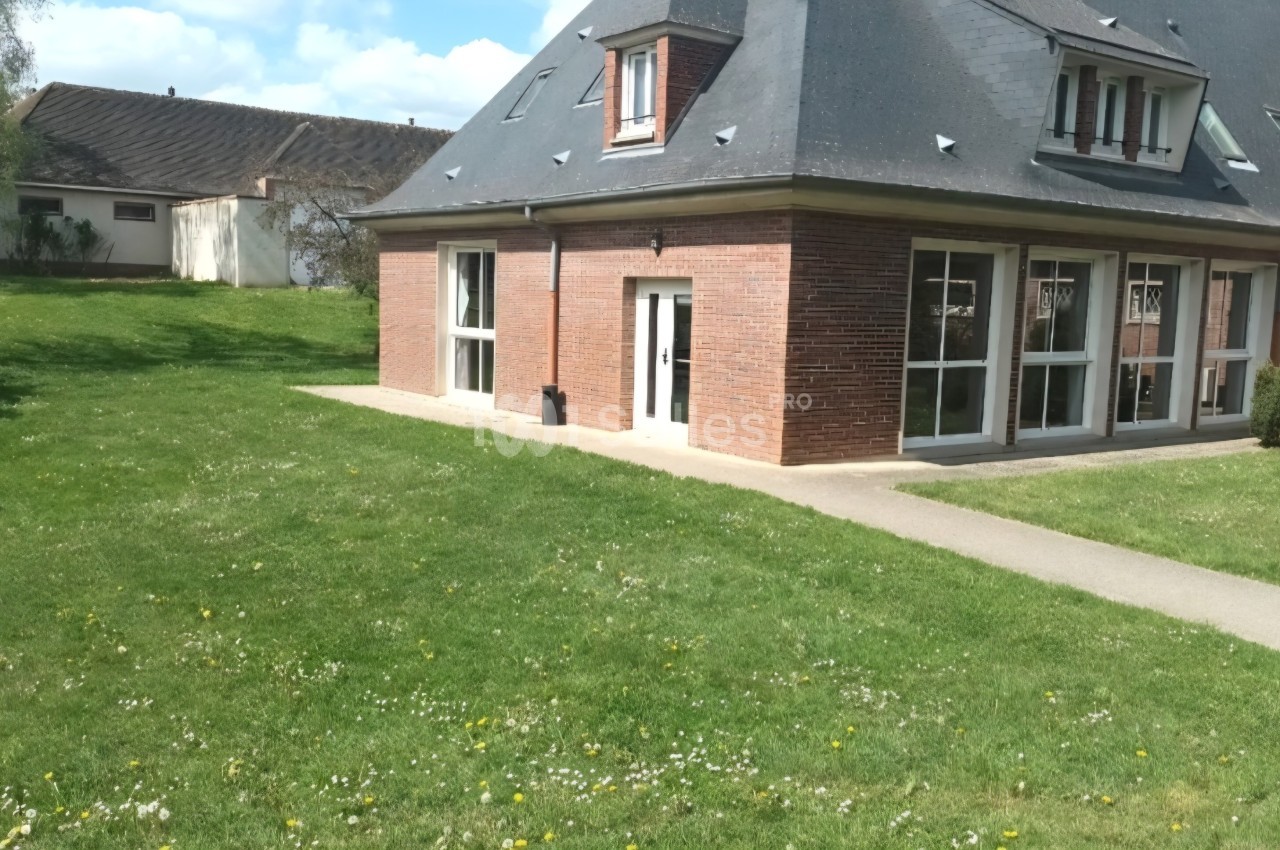 Maison en briques avec toit en ardoise, entourée d'une pelouse et d'un chemin pavé sous un ciel dégagé.