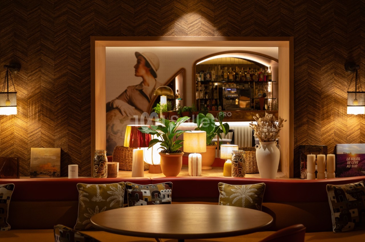 Intérieur de bar au design rétro avec comptoir éclairé, tabourets à motifs floraux et rangées de bouteilles en arrière-plan.