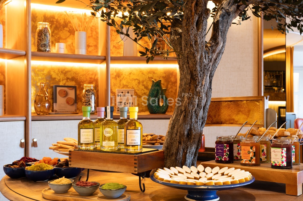 Buffet gastronomique avec huiles d'olive, pains, fromages et accompagnements sous un olivier ancien et éclairage chaud.