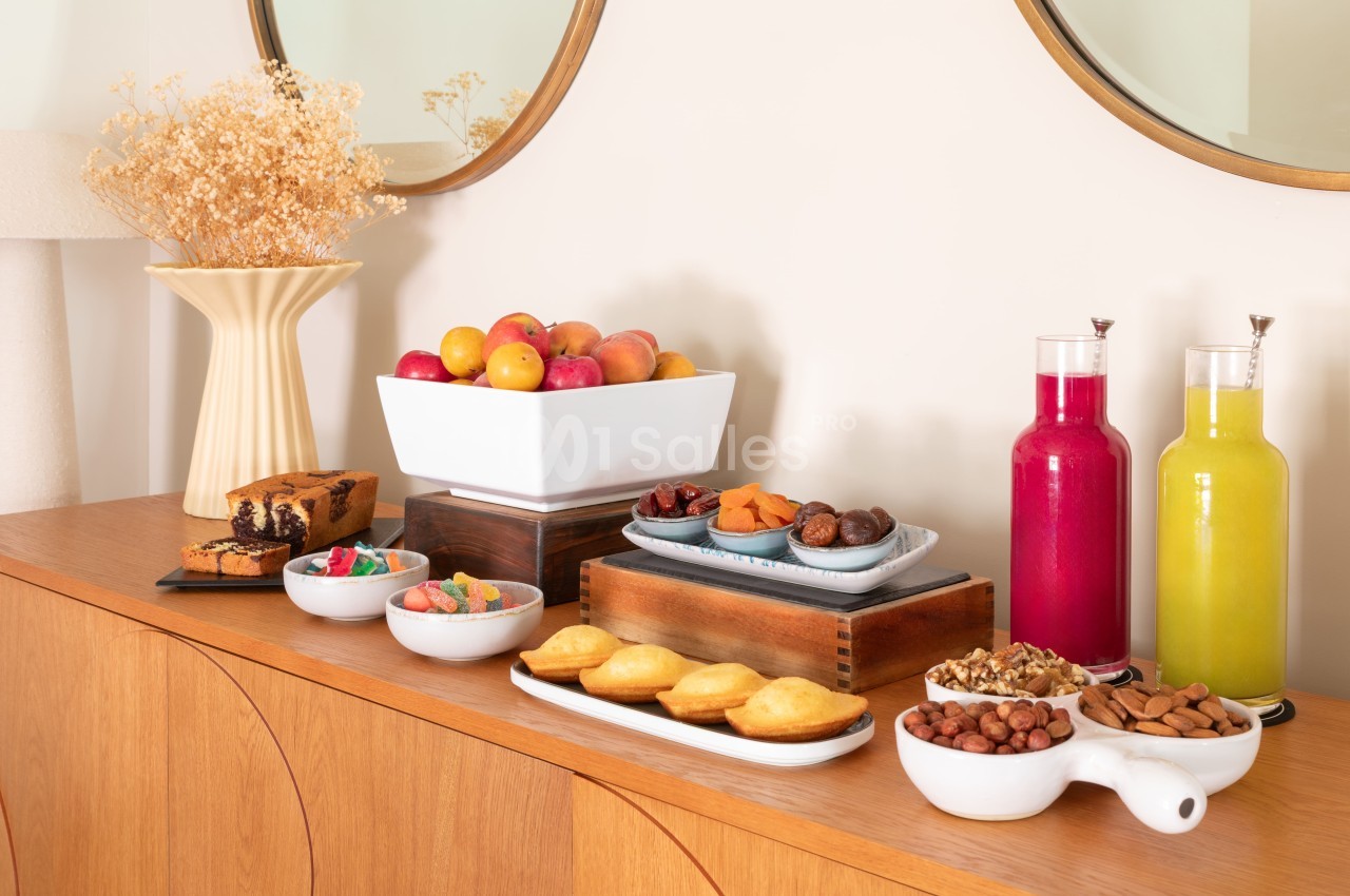 Buffet de réception avec fruits, pâtisseries, fruits secs, jus de fruits et décoration florale sur table en bois.