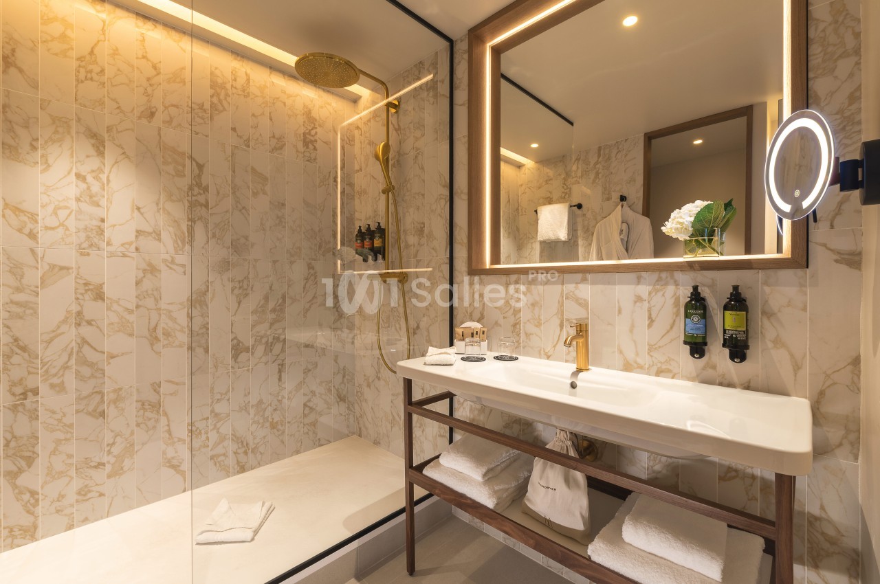 Salle de bains avec douche à l'italienne vitrée, vasque blanche, miroir éclairé et marbre clair.