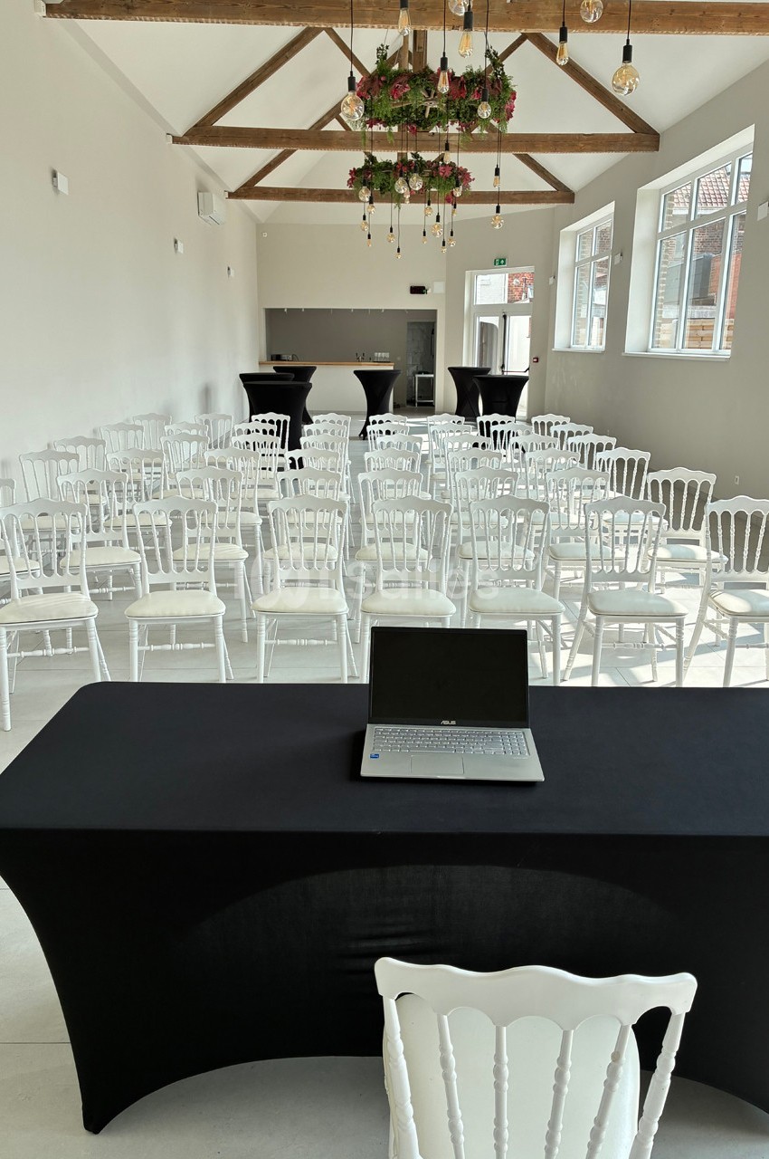 Salle lumineuse aménagée pour une conférence, avec des rangées de chaises blanches et une table noire équipée d'un…