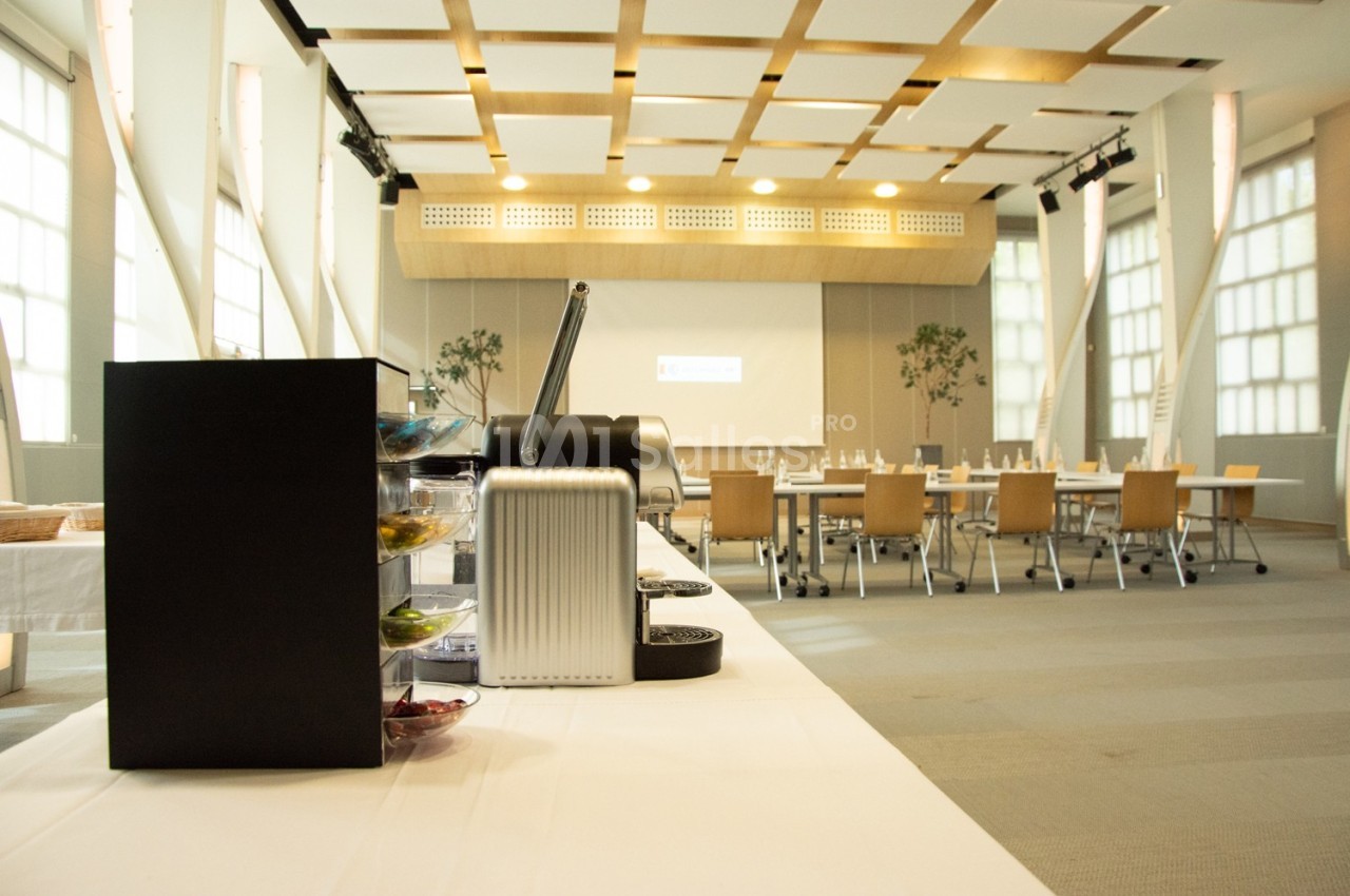 Machine à café sur une table en premier plan, avec une salle de réunion lumineuse et aménagée en arrière-plan.