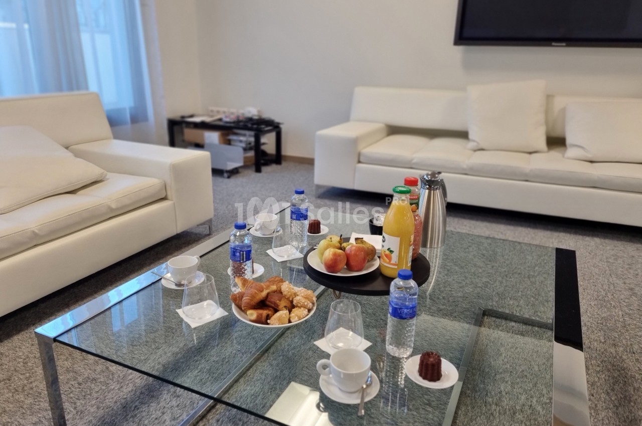Petit-déjeuner servi sur une table basse en verre avec viennoiseries, fruits, jus, café et bouteilles d'eau.