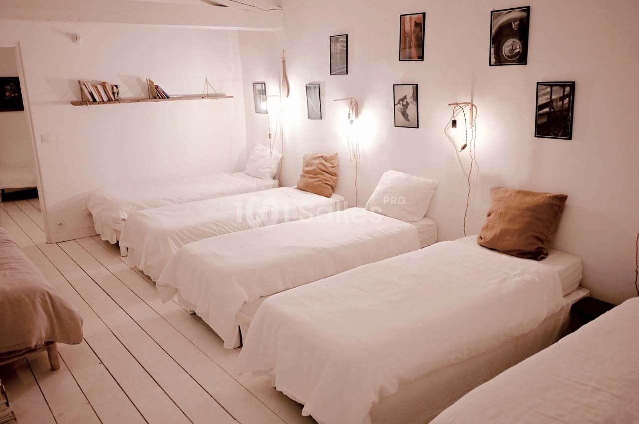 Chambre lumineuse avec cinq lits simples alignés, décorée de cadres, étagères et éclairages muraux.