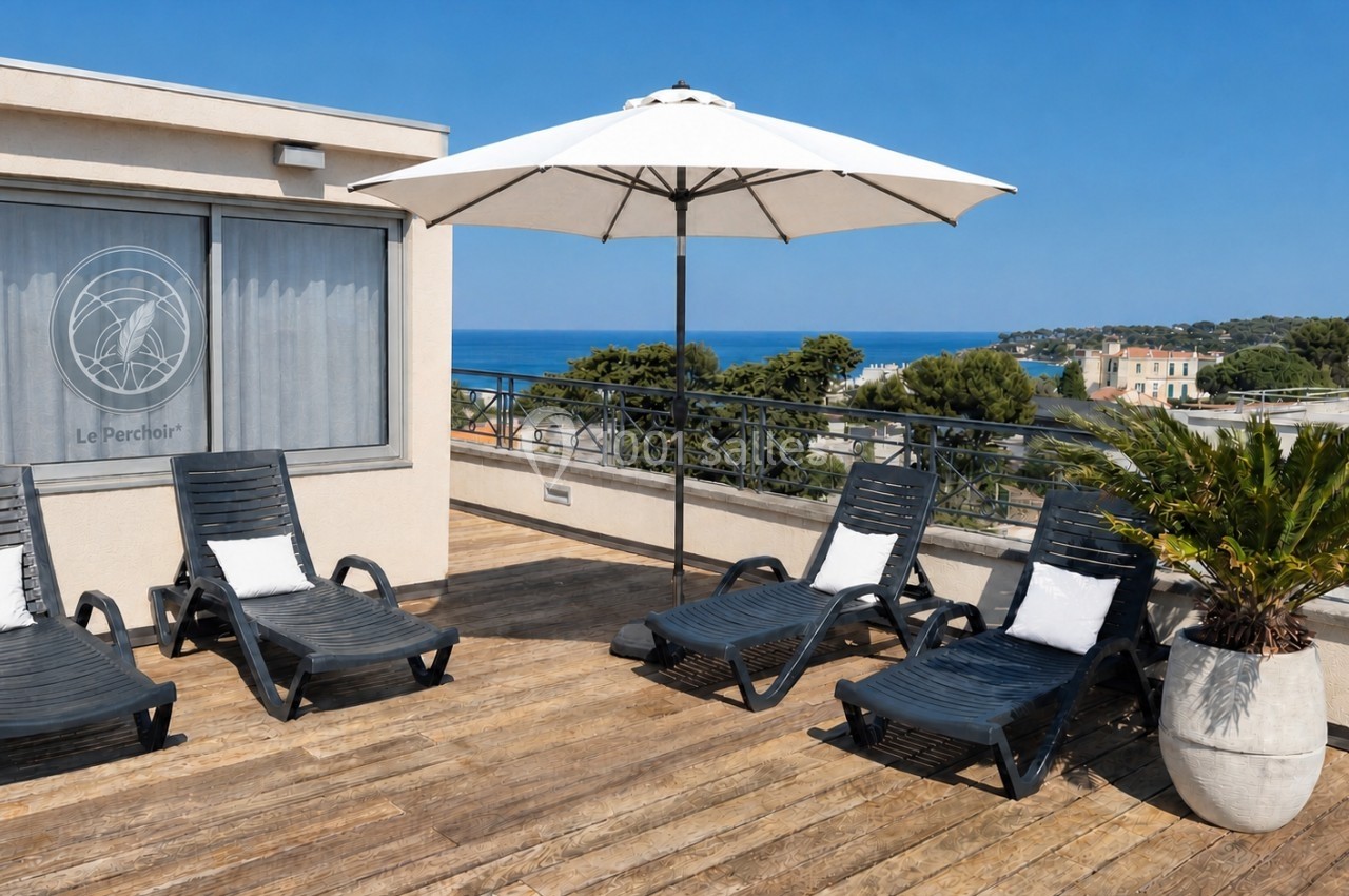 Terrasse en bois avec chaises longues, parasol blanc, plante en pot et vue sur la mer et la végétation environnante.