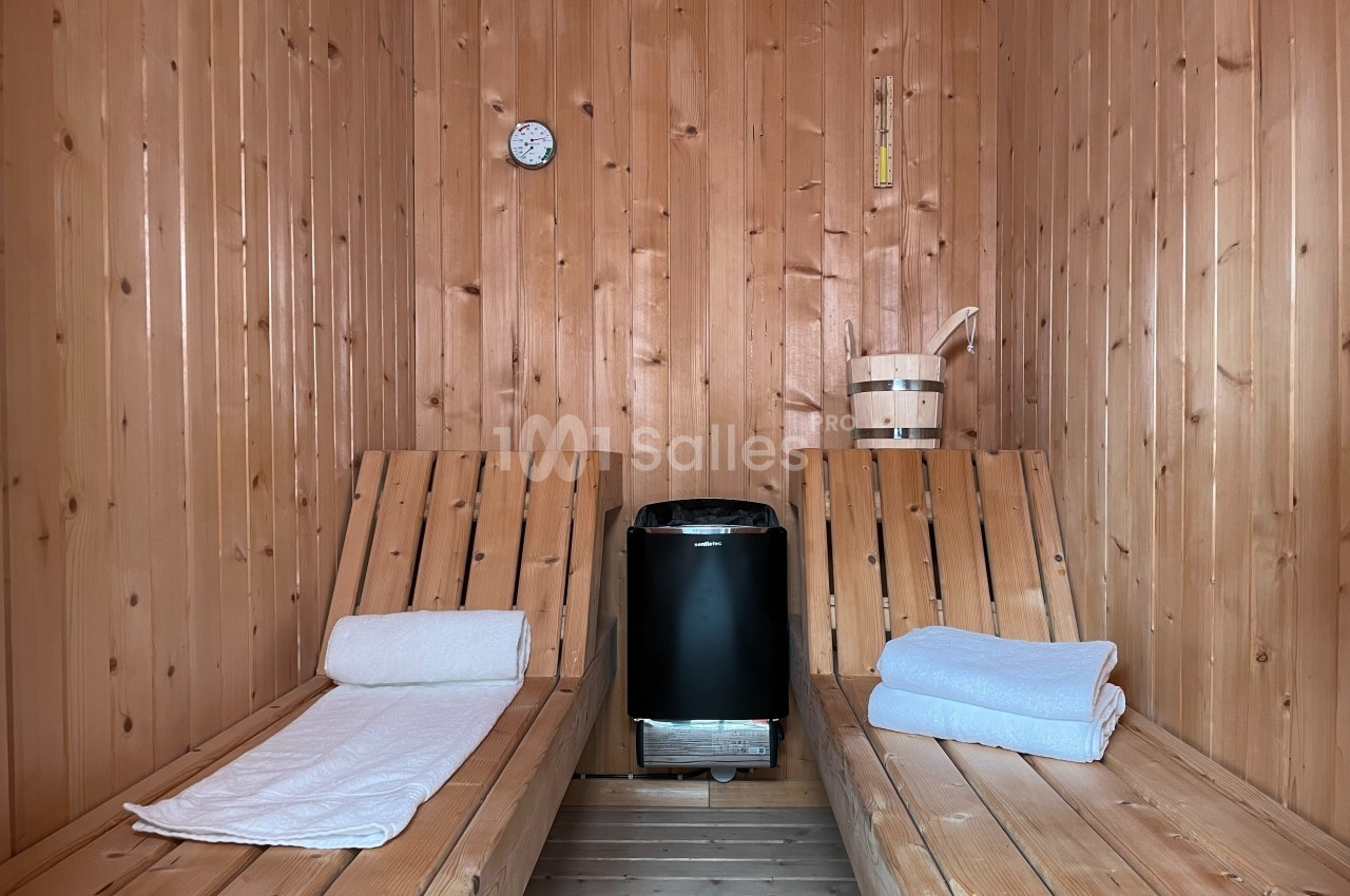 Intérieur d'un sauna en bois avec deux bancs, des serviettes pliées et un poêle au centre.