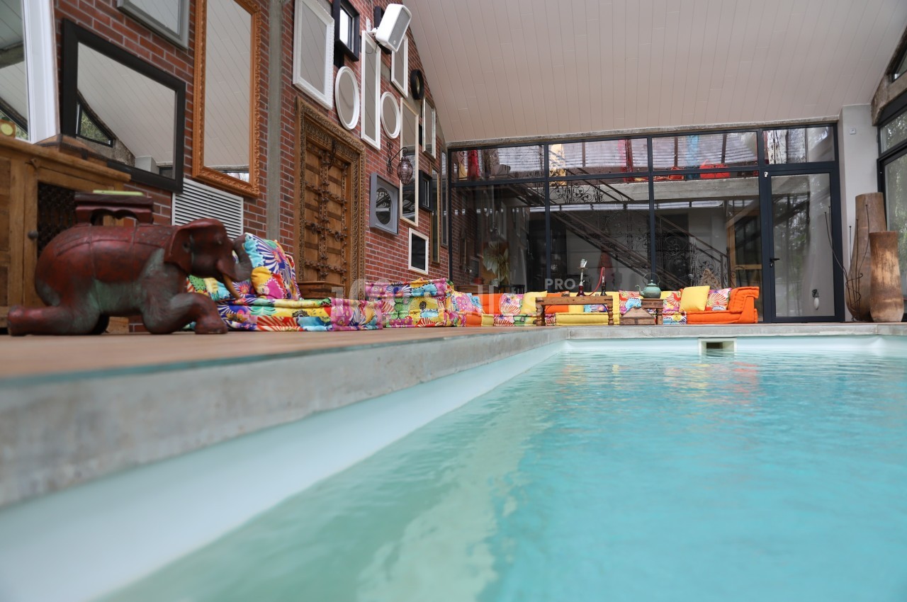 Piscine intérieure bordée de canapés colorés et de décorations éclectiques dans un espace lumineux avec murs en verre.