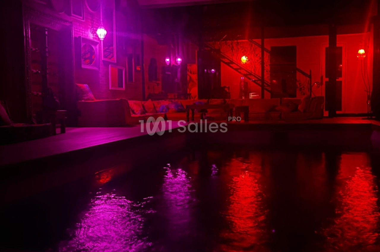 Espace intérieur avec piscine éclairée par des lumières rouges et violettes, ambiance tamisée et chaleureuse.