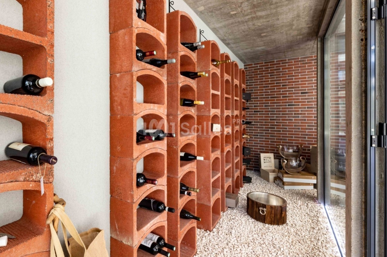 Cave à vin avec étagères en briques rouges, bouteilles rangées et sol recouvert de gravier blanc.