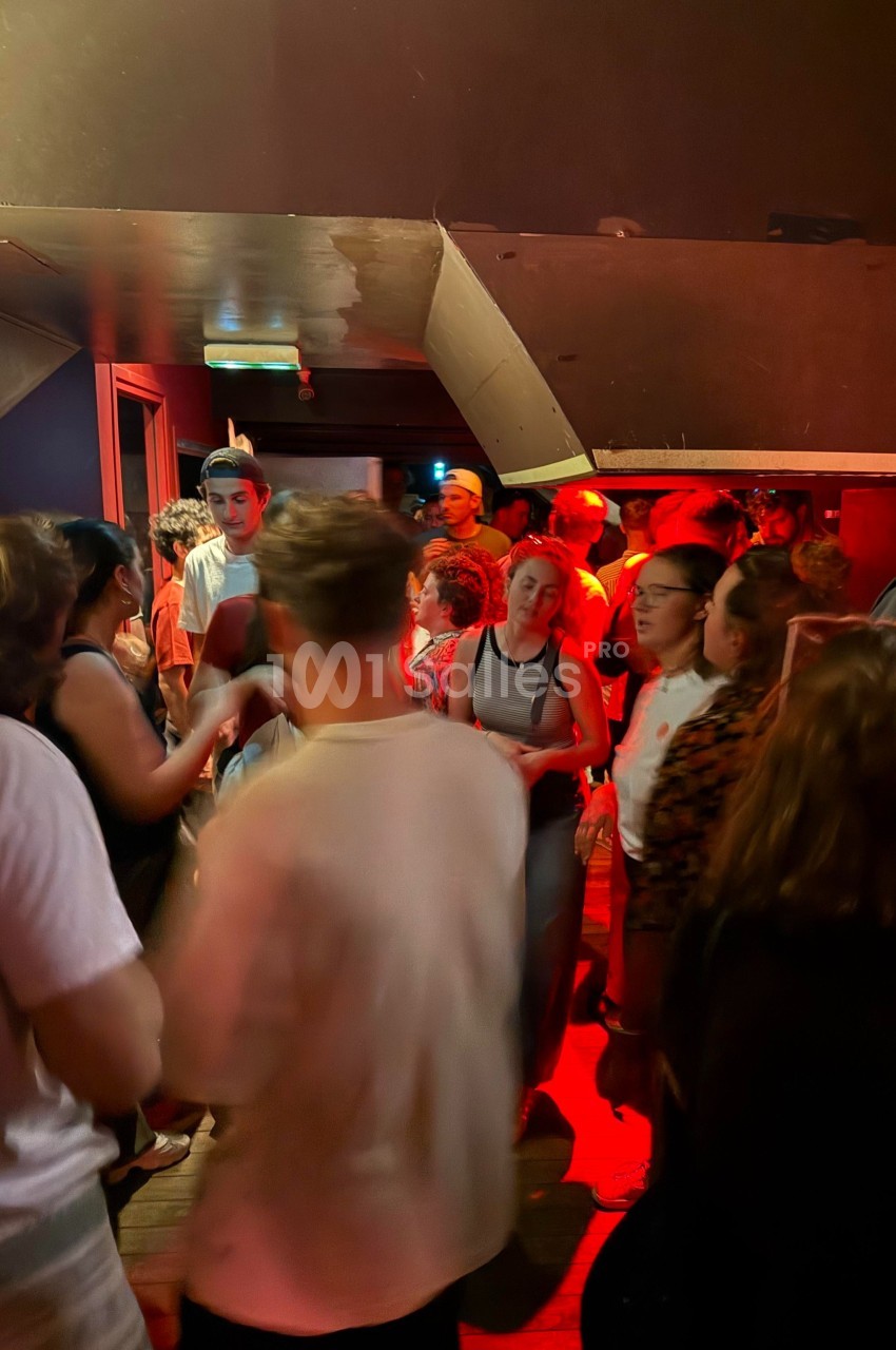 Personnes discutant et se déplaçant dans un espace intérieur faiblement éclairé avec une lumière rouge dominante.