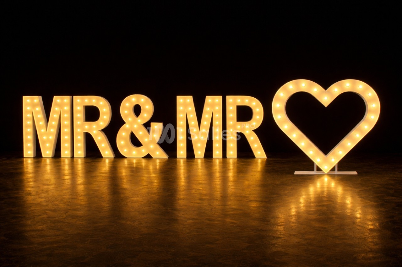 Lettres lumineuses ’MR & MR’ avec un cœur éclairé, posées sur un sol sombre dans un environnement obscur.