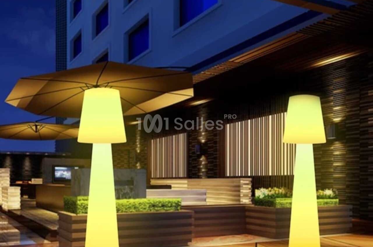 Terrasse moderne éclairée de nuit avec des lampes jaunes en forme de colonnes et des parasols.