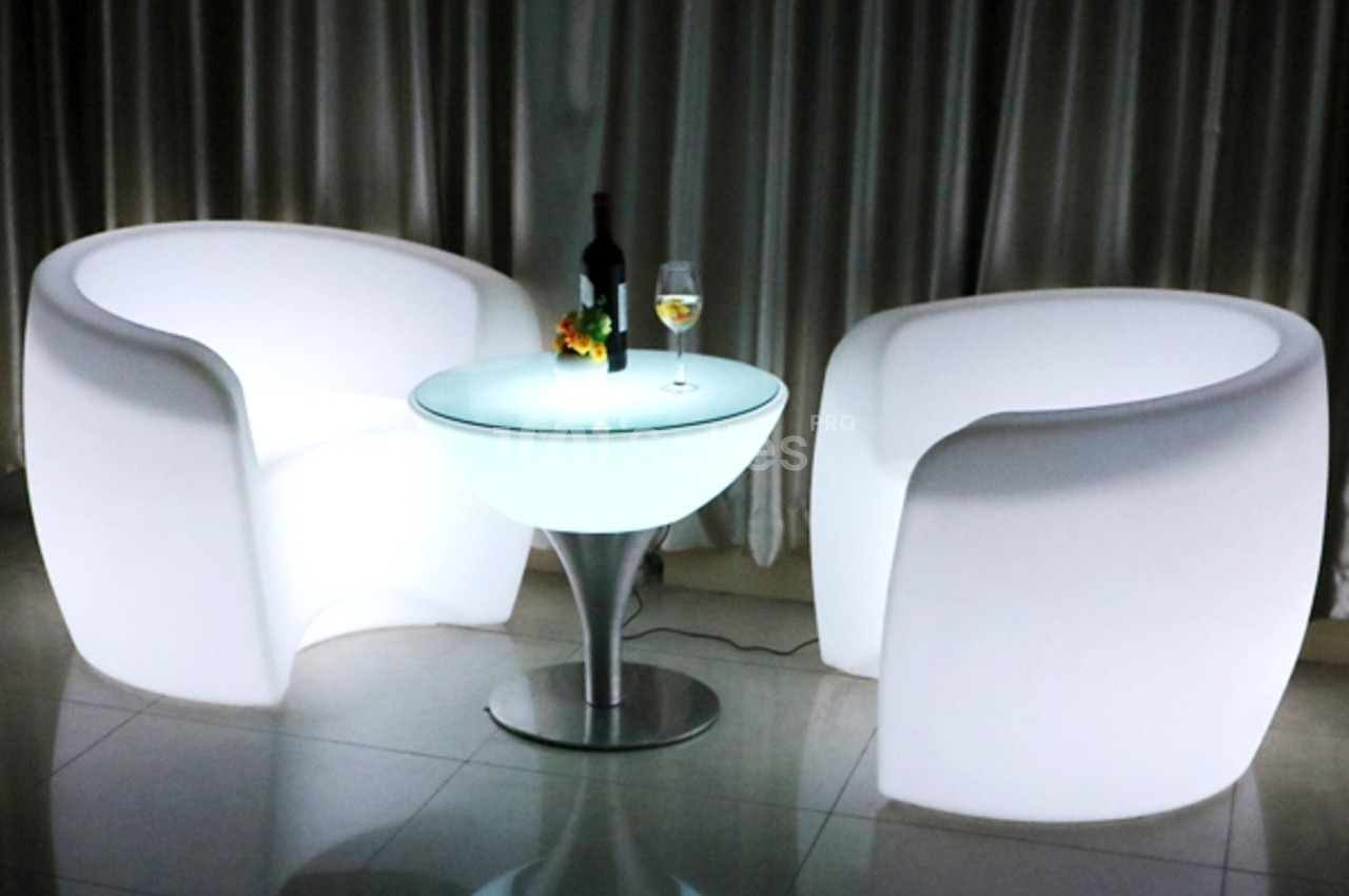 Deux fauteuils lumineux blancs entourant une table ronde éclairée, avec une bouteille de vin et un verre dessus.