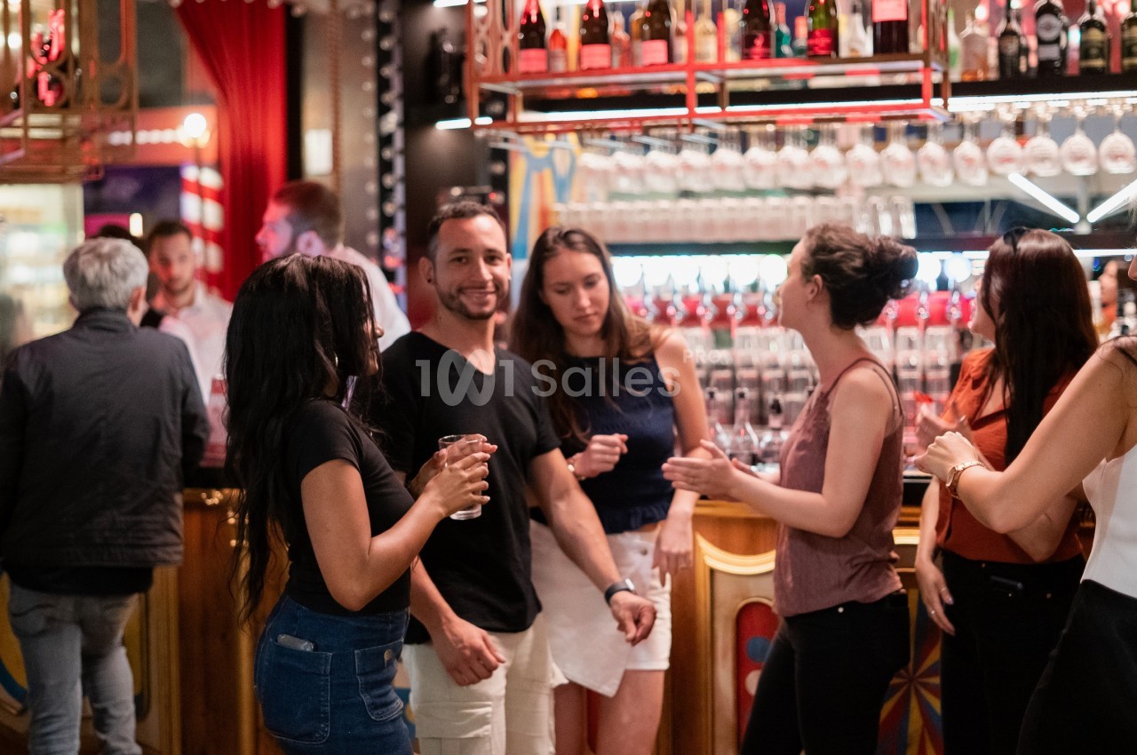 Des personnes discutent et partagent un moment convivial autour d'un bar lumineux et décoré.