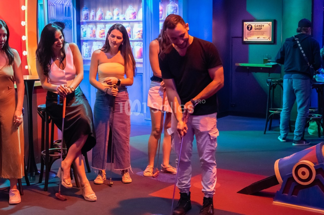 Un groupe de personnes regarde un homme jouer au mini-golf dans un espace coloré et lumineux.