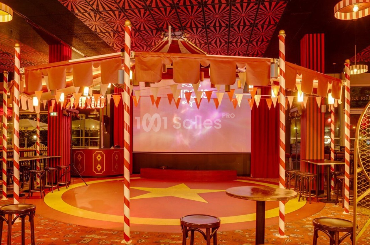 Intérieur d'une salle décorée sur le thème du cirque avec chapiteau, étoile au sol et chaises disposées autour.