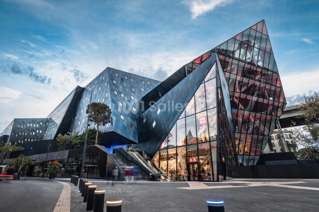 Façade moderne d'un bâtiment en verre et métal avec des formes angulaires, entouré d'un espace urbain.