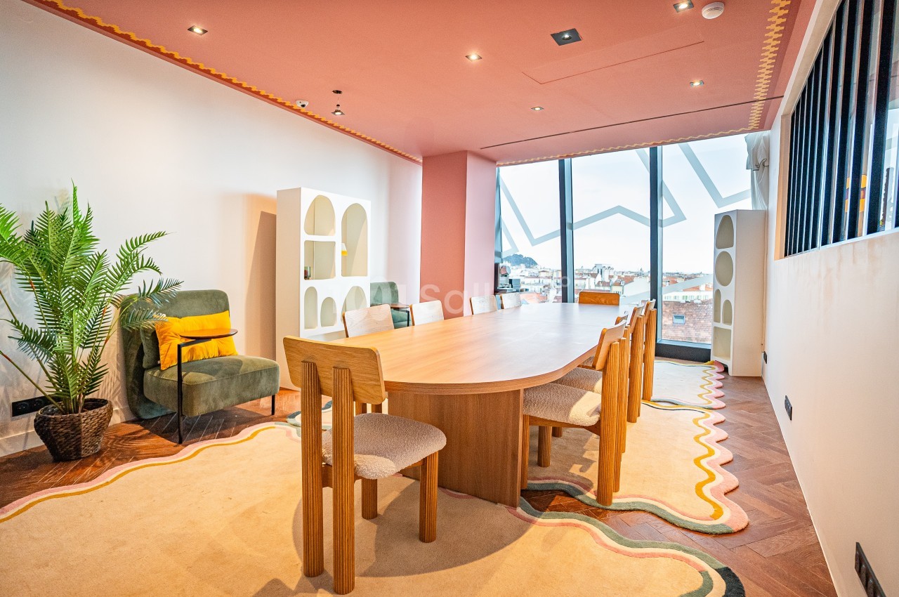 Salle de réunion lumineuse avec une grande table en bois, des chaises, un fauteuil vert et une plante décorative.