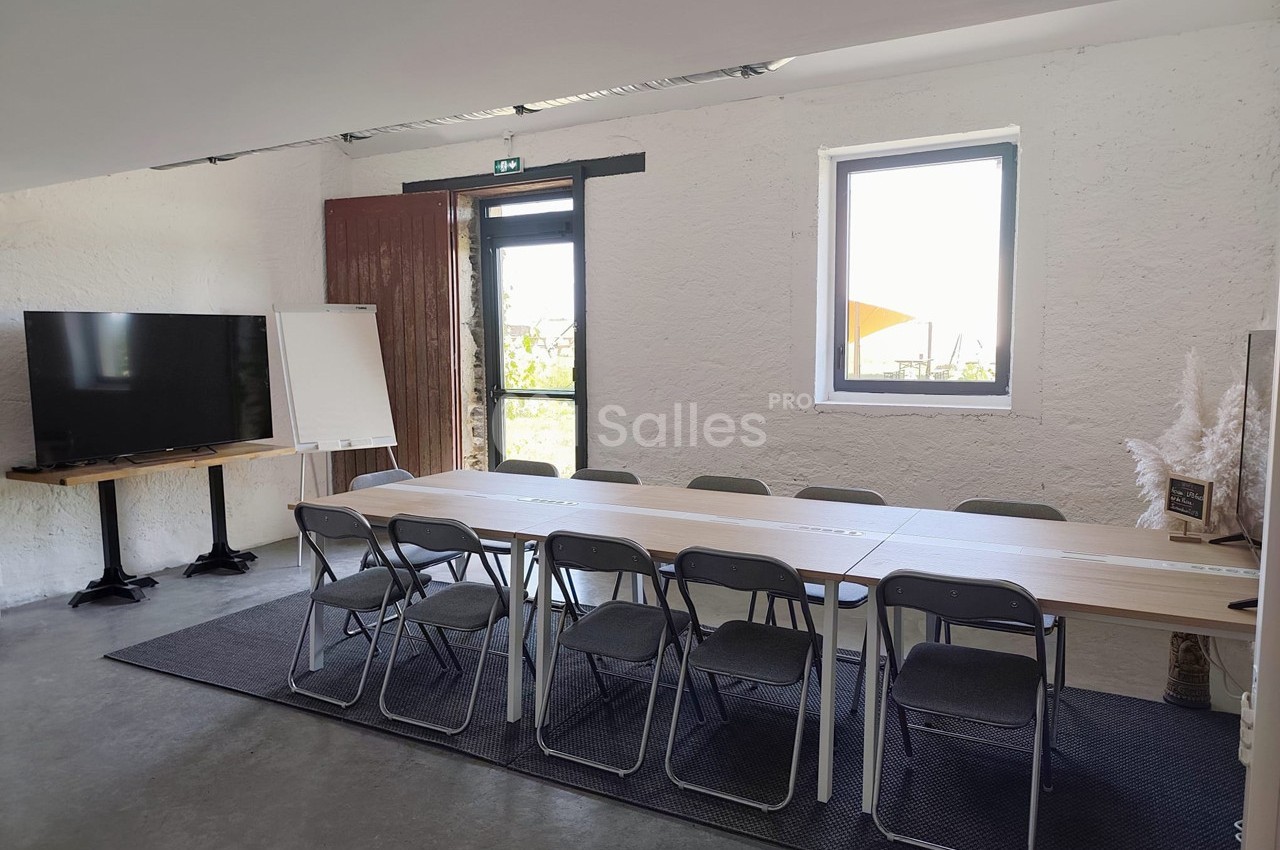 Salle de réunion lumineuse avec une grande table, des chaises, un tableau blanc et un écran près d'une fenêtre.