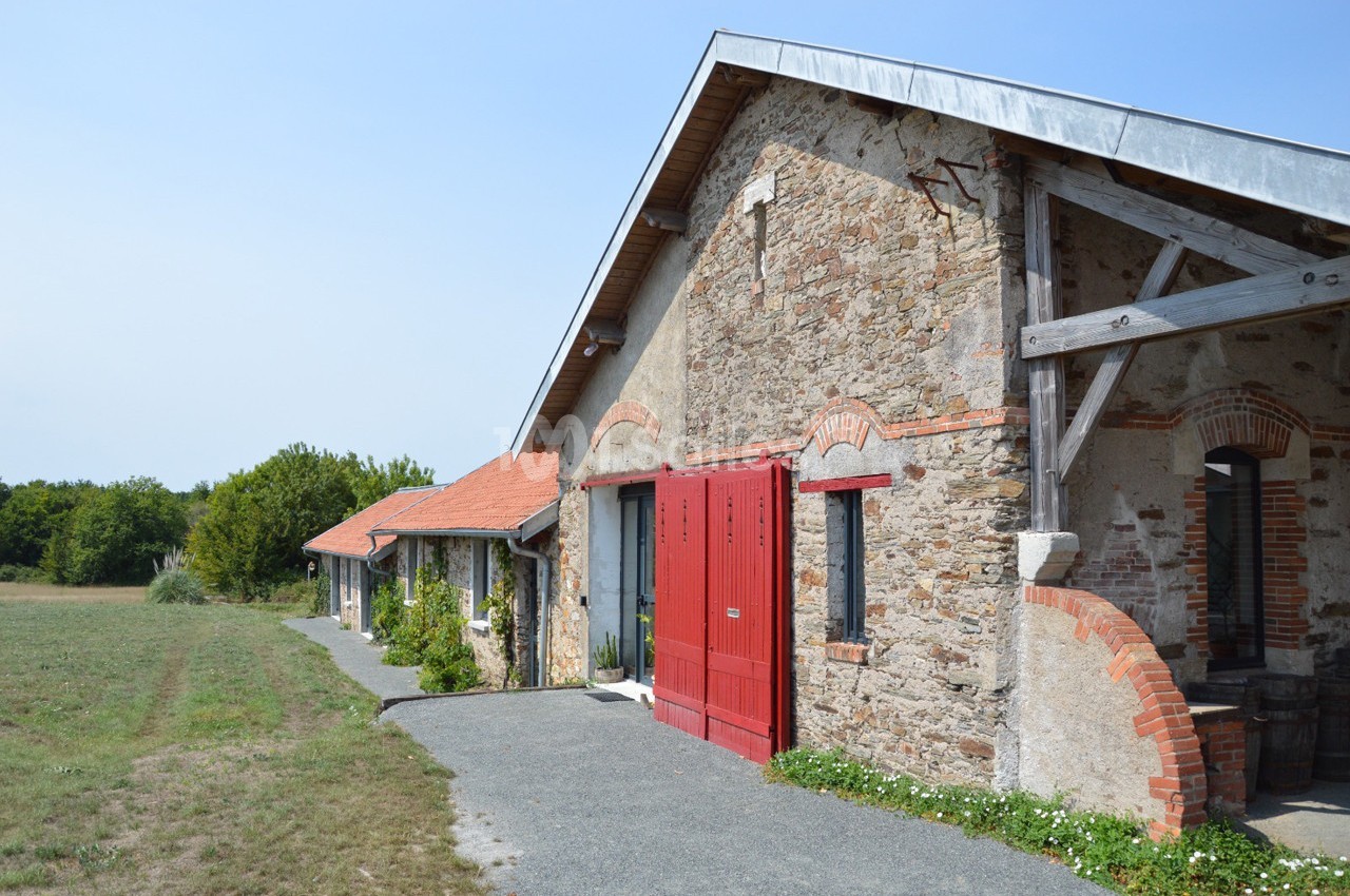 Bâtiment en pierre avec portes rouges, toit en tuiles et poutres en bois, entouré de végétation et d'un chemin pavé.
