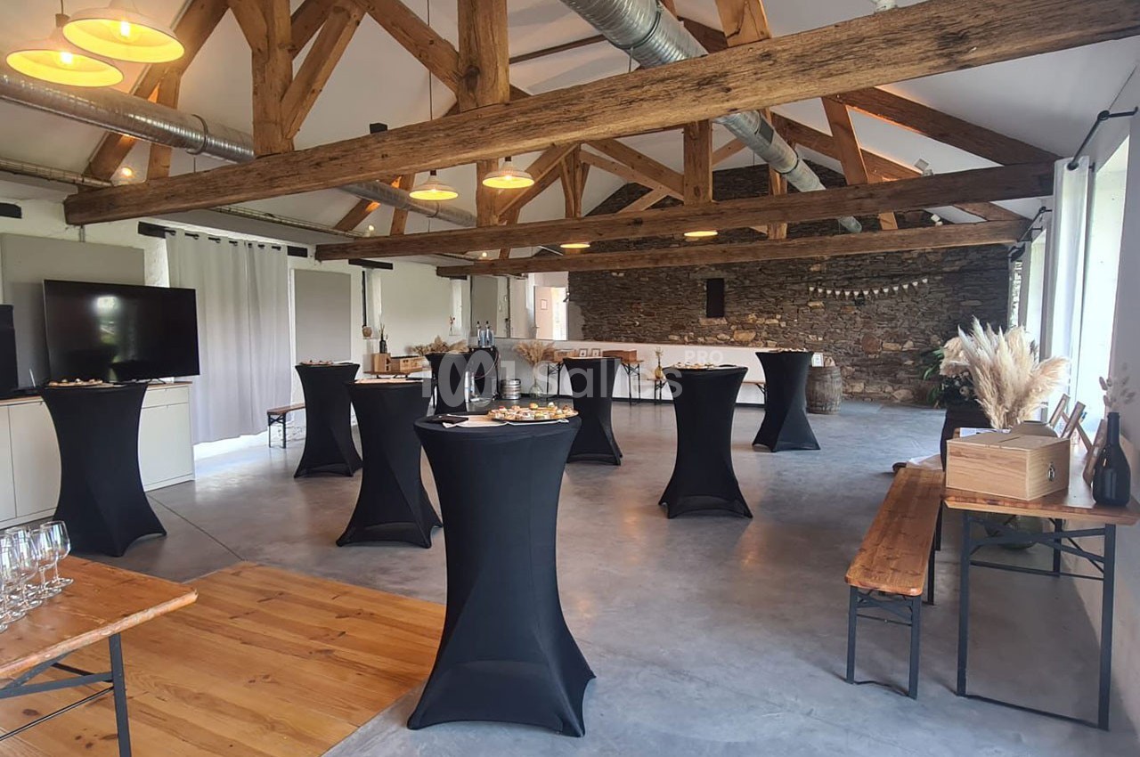 Salle de réception avec poutres apparentes, tables hautes noires et buffet disposé le long d'un mur en pierre.