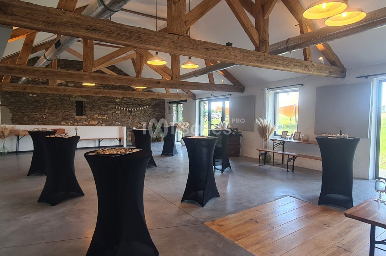 Salle lumineuse avec poutres apparentes, tables hautes drapées de noir et décorations minimalistes.